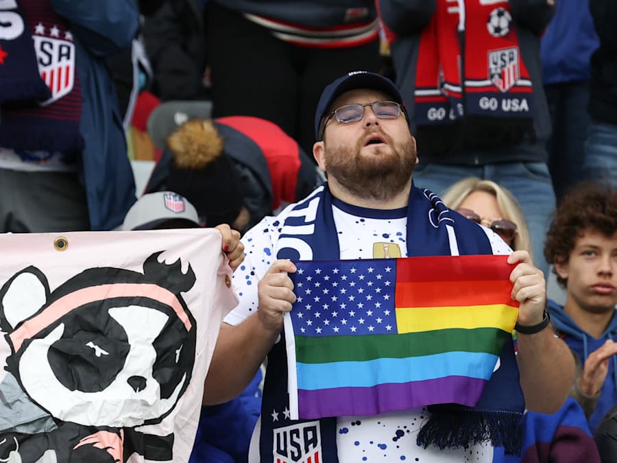 A man holds a LGBTQ+ flag at a USA soccer match
