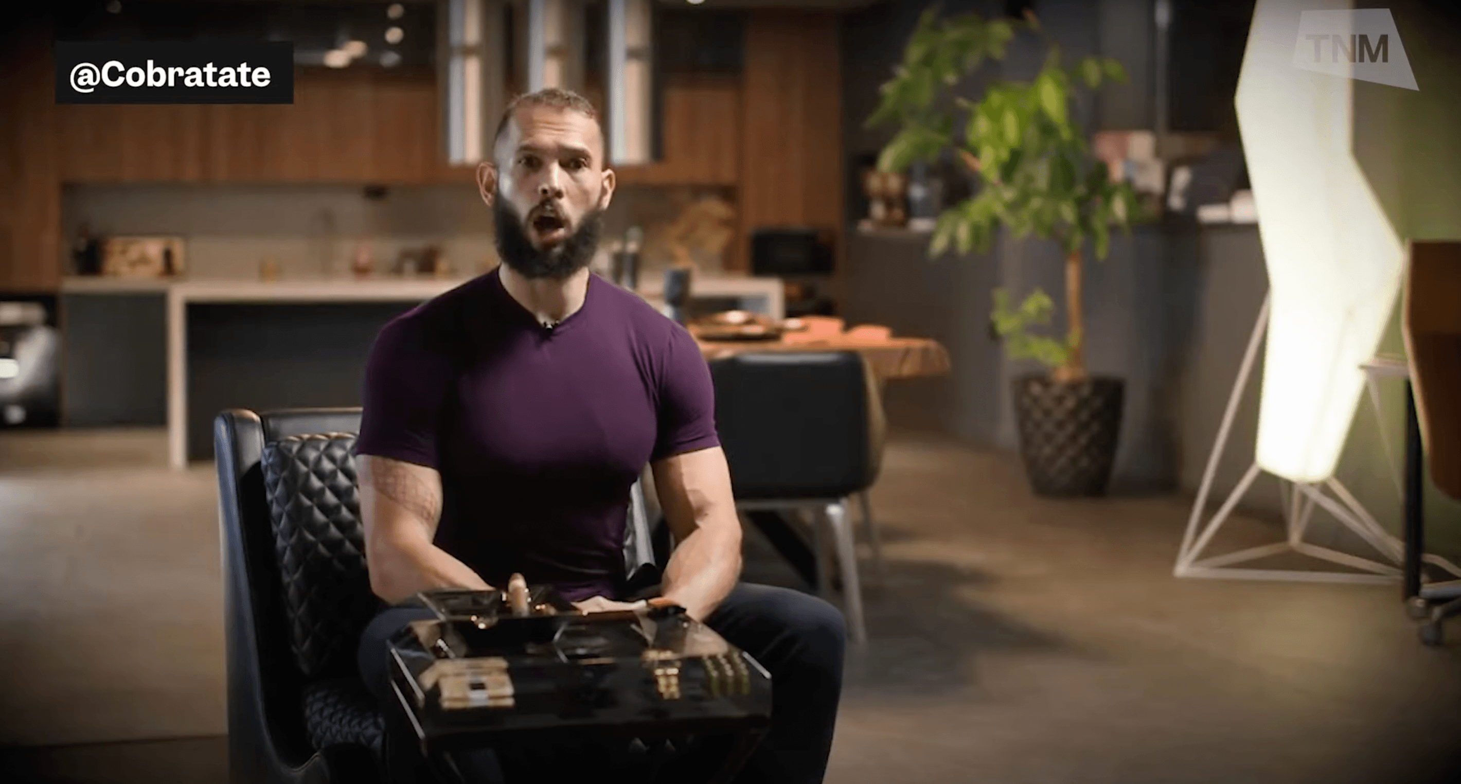 Andrew Tate in a maroon shirt in a warehouse like building 